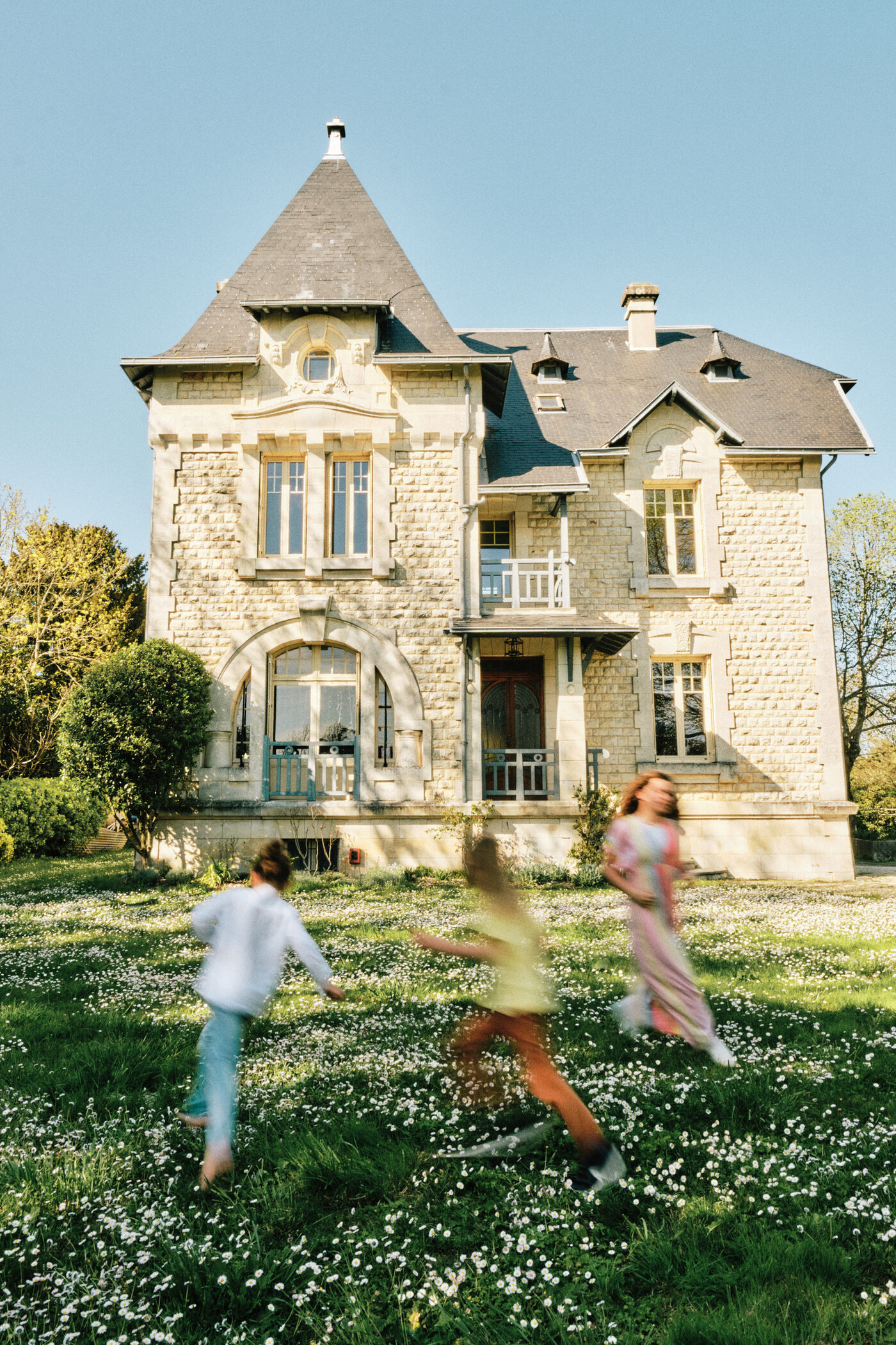L’autre face de la Villa Nymphea, la tourelle de pierre, et trois enfants qui courent dans la pelouse pleine de pâquerettes