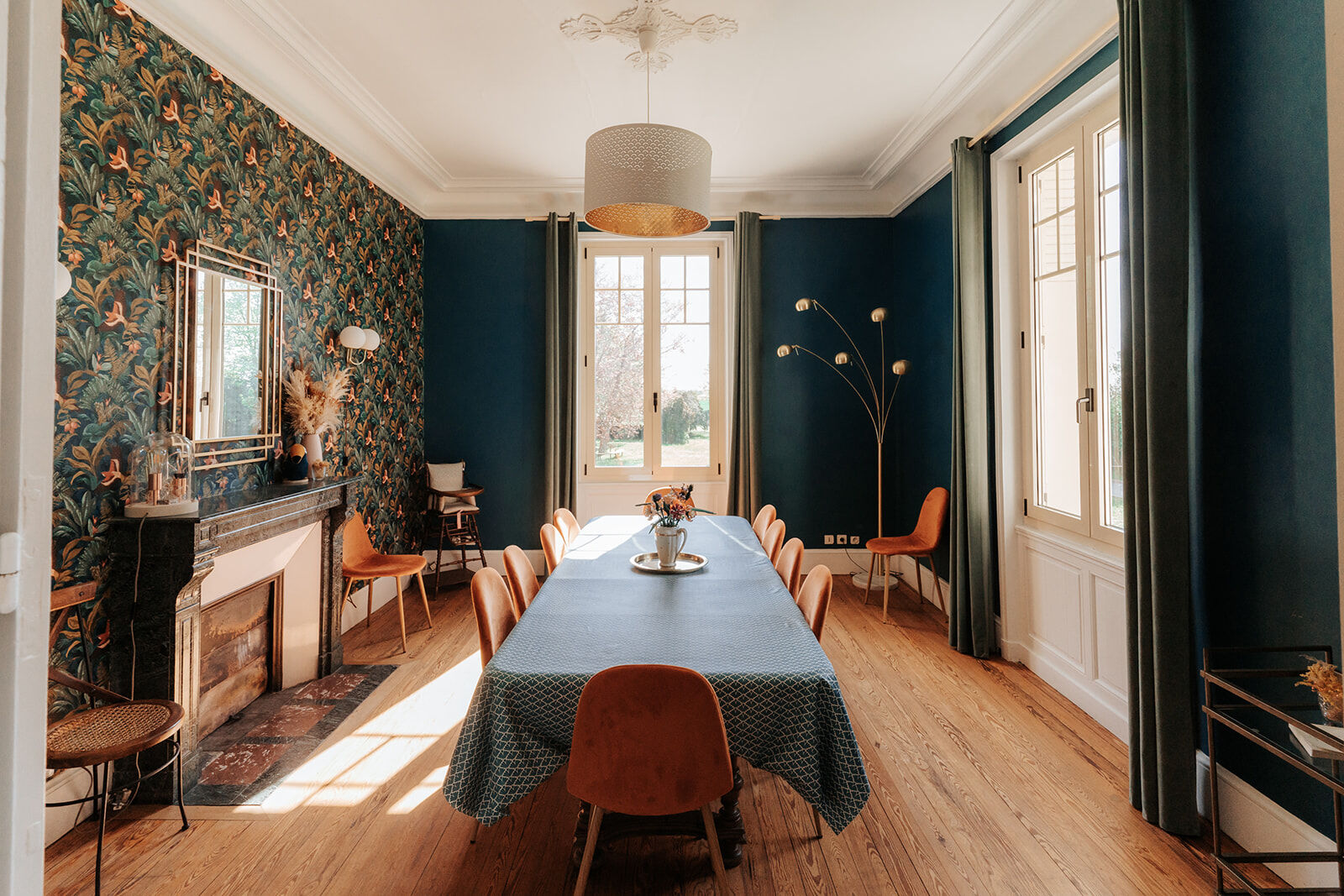 La salle à manger de la Villa Nymphea, murs bleu profond et papier peint fleuri, la grande table sous sa nappe avec un bouquet au milieu